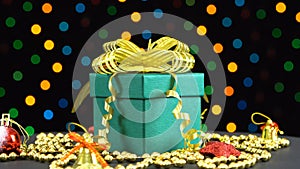 Beautiful Christmas green gift box with golden bow and decorations rotating against colorful flashing garland on a black