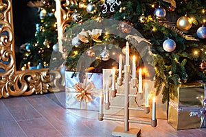 Beautiful Christmas interior. A Christmas tree with gold ornaments, boxes with gifts, and a candelabrum with burning