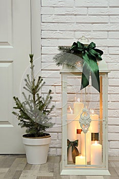 Beautiful Christmas lantern and potted fir tree near entrance indoors