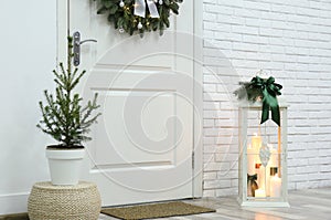 Beautiful Christmas lantern and potted fir tree near entrance indoors