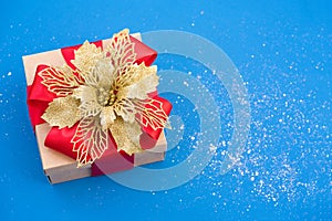 Beautiful Christmas present box with red ribbon bow and traditional decorative Christmas flower poinsettia on blue