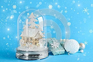 Beautiful Christmas snow globe, gift box and ornaments on light blue background, bokeh effect. Space for text