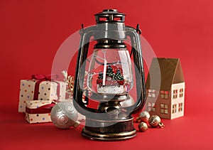Beautiful Christmas snow globe, gift boxes and festive decor in vintage lantern on red background