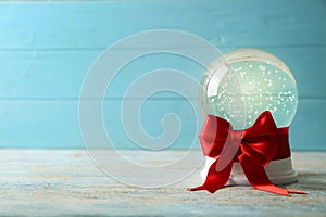 Beautiful Christmas snow globe with red bow on white wooden table against blue background