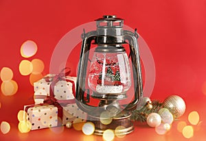 Beautiful Christmas snow globe in vintage lantern, gift boxes and decor on red background, bokeh effect