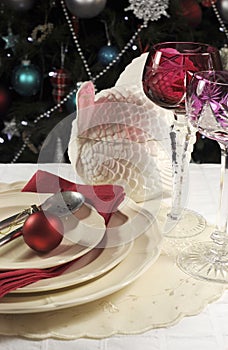 Beautiful Christmas table setting in front of Christmas Tree, with red crystal wine goblet glasses - vertical