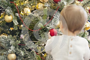 Beautiful Christmas tree with golden and red decoration. Image out of focus of a little girl from behind holding red ball