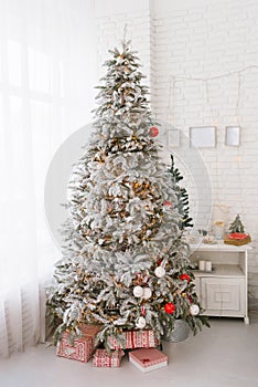 Beautiful Christmas tree with toys and gifts in the interior of a bright room at home by the window