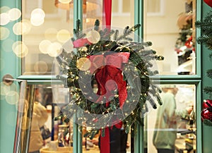 Beautiful Christmas wreath with ribbon and festive lights hanging on door