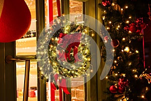 Beautiful Christmas wreath with ribbons and festive lights hanging on door