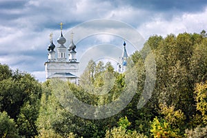 Beautiful church with domes in the dense green foliage of trees. Against the background of a blue cloudy sky