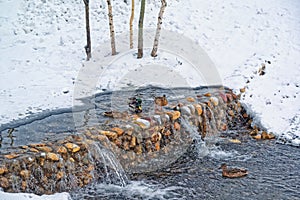 Beautiful city park on the outskirts of the city. Winter, gloomy sky and heavy snow. Ducks hibernate in an unfrozen stream