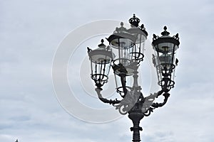 Beautiful classic iron lamppost of six lamps with diode bulbs against a cloudy sky in a European city