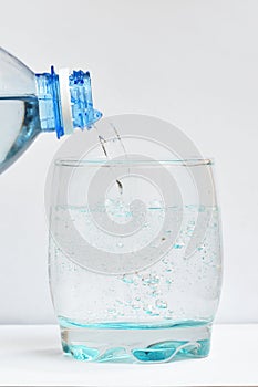 Beautiful and clean drinking water is poured into a transparent glass. Pouring water from bottle into glass on blue background