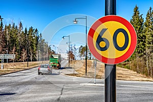 Beautiful close up photo of fresh 60 km speed limit traffic sign mounted on black pole. Blurry background with one car and truck