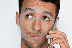 Portrait of young handsome uncertain man using mobile phone on gray background. Businessman confuse speaking on his smart phone