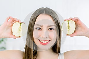 Beautiful close-up portrait of young woman with halfs of an apple. Healthy food concept. Skin care and beauty. Vitamins