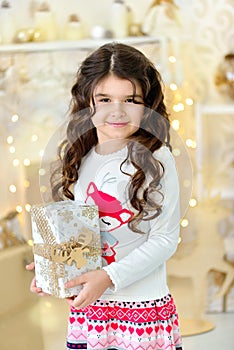 Beautiful close up portraite of curly girl with gold Christmas garlands magic lights and tree decorations gift box