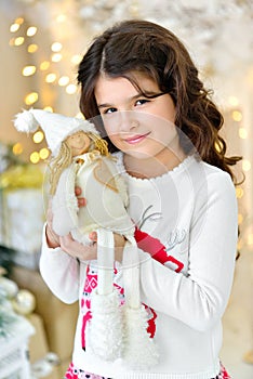 Beautiful close up portraite of curly girl with gold Christmas garlands magic lights and tree decorations hugs toy angel