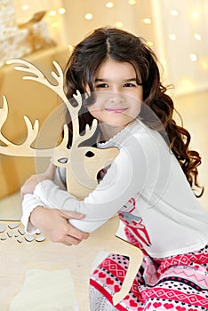 Beautiful close up portraite of curly girl with gold Christmas garlands magic lights and tree decorations hugs toy deer