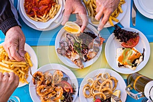 Beautiful close up of table woth gourmet and marine food like fish and chips with hands taking it - group of people eating