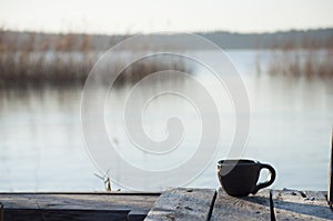 Beautiful closeup of unique handmade cup with blurred lake on background. Black pottery in Latvia nature.