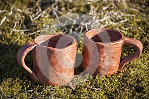 Beautiful closeup of unique handmade two cups with folk signs on green moss in summer sunset sunlight before kiln