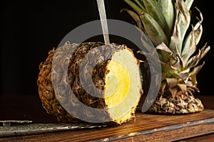 Beautiful closeupshot of a pineapple with its cut crown on a wooden board with sharp vintage knifes