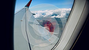 Beautiful clouds and an airplane wing out of a window with a beautiful blue sky. Shot from the porthole of an airplane