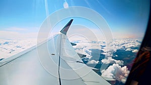 Beautiful clouds and an airplane wing out of a window with a beautiful blue sky. Shot from the porthole of an airplane