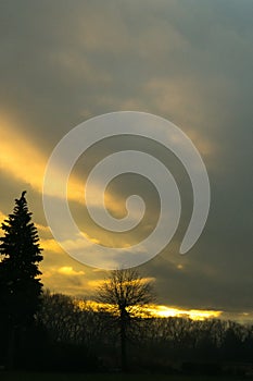 Beautiful clouds over the green meadow, paths and trees, during sunrise or sunset.