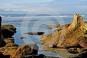 Beautiful coastline with rocks in the foreground and volcanic mountains at the background. Bali, Indonesia