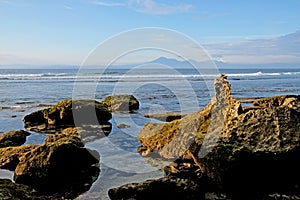 Beautiful coastline with rocks in the foreground and volcanic mountains at the background. Bali, Indonesia