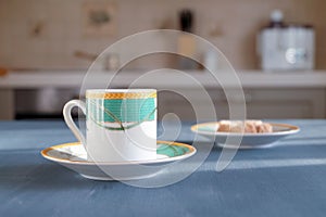 A beautiful coffee cup stands on a dark gray surface on a blurry background of the kitchen interior