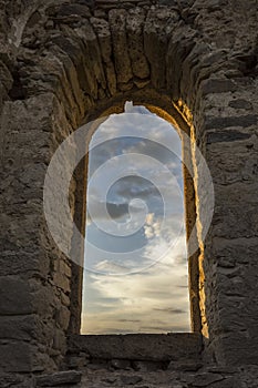 Beautiful colorful clouds on blue sky on sunset. View through arched window in old stone abandoned church. ÃÂrchitecture photo