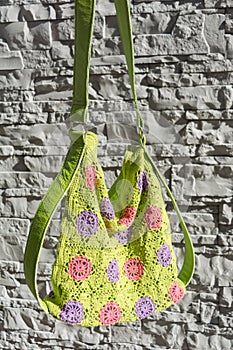 Beautiful colorful crocheted handbag with green handle behind the gray stone wall in the garden in summer