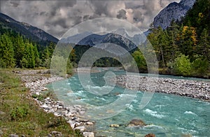 Beautiful colorful landscape with a stream and forest, mountains in the background and cloudy sky.