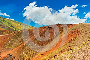 Beautiful colorful lava hills with group of people hiking to a volcanic crater. Mount Etna, Sicily, Italy