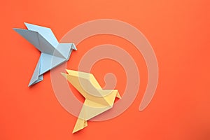 Beautiful colorful origami birds on orange background, flat lay. Space for text