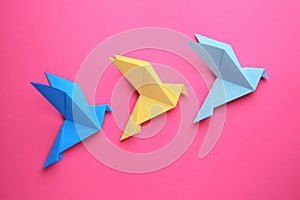 Beautiful colorful origami birds on pink background, flat lay