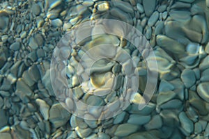 Beautiful colorful pebbles and big stone under turquoise blue clear water, scenic marine background or texture, top view