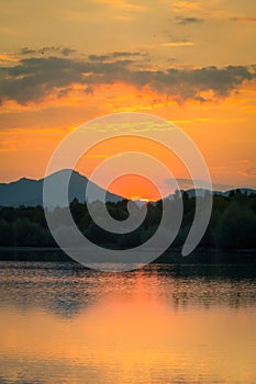 A beautiful, colorful sunset landscape with lake, mountain and forest. Natural evening scenery over the mountain lake in summer.