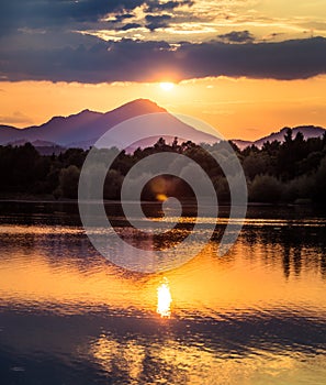 A beautiful, colorful sunset over the mountains, lake and forest in purple tones. Abstract, bright landscape.