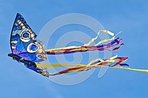 A beautiful, colourful stunt kite, in the blue sky, high up in the wind in form of a butterfly