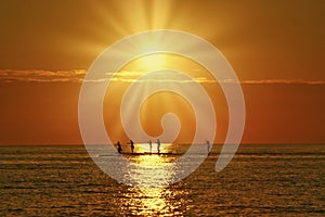 Paddleboarders in the path of the sun as the sun goes down photo