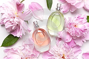 Beautiful composition with perfume and flowers. Perfume bottle, pink flowers peonies green leaves on light background top view