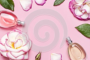 Beautiful composition with perfume and flowers. Perfume bottles, rose flowers petals green leaves on pink background top view Flat