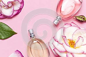 Beautiful composition with perfume and flowers. Perfume bottles, rose flowers petals green leaves on pink background top view Flat