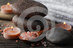 Beautiful composition with spa stones and burning candles on wooden table, closeup