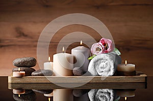 Beautiful composition with spa stones, flowers and burning candles on mirror table against wooden background